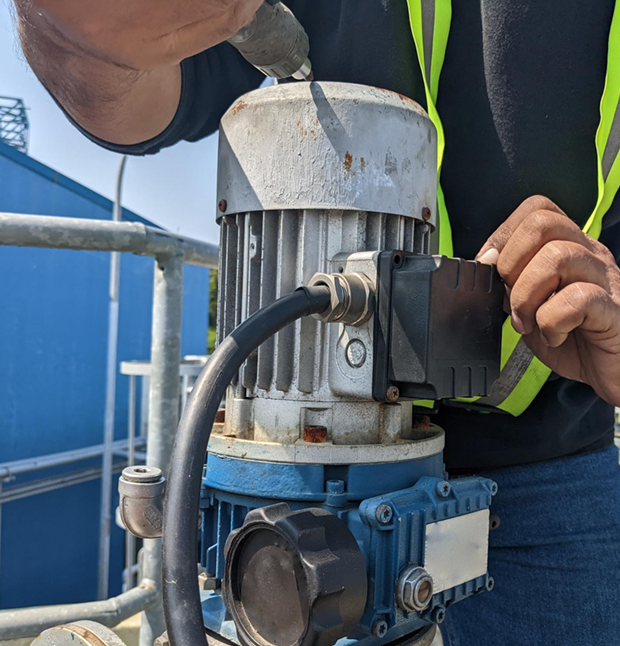 Person in a safety vest working on a blue pump motor outdoors.