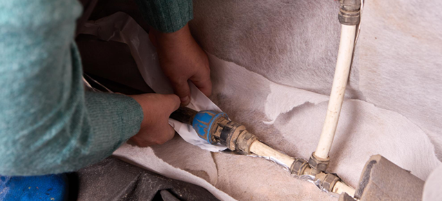 Person working on a water pipe. Hands are holding a connector, likely repairing a leak. White pipes.