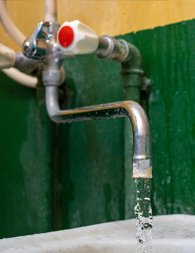 Faucet with water running, against a green wall. White and red valve on top.