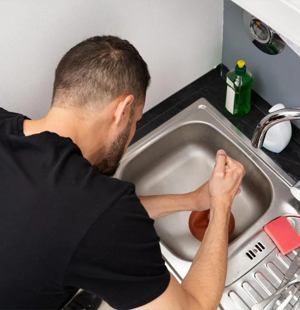 Man uses a plunger in a kitchen sink to unclog a drain.