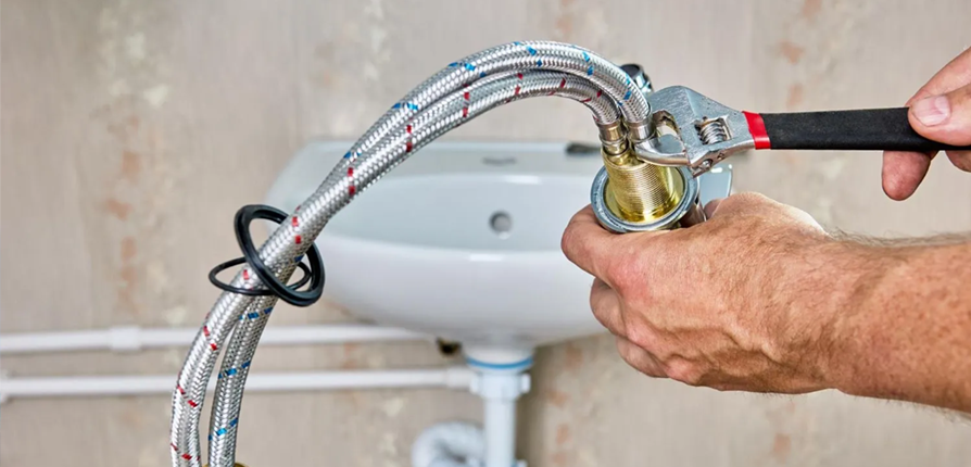 Person using a wrench to connect a flexible hose to a sink's faucet fitting.