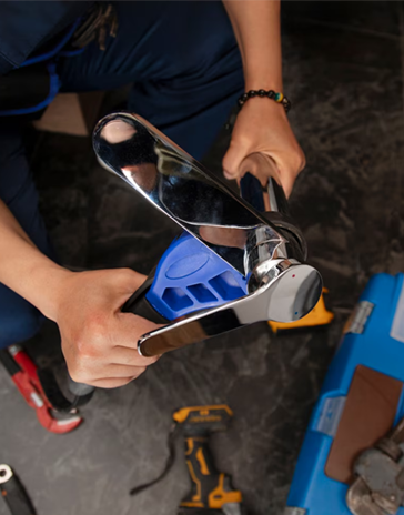 Person using a crimping tool on a blue component, with tools visible on a dark floor.