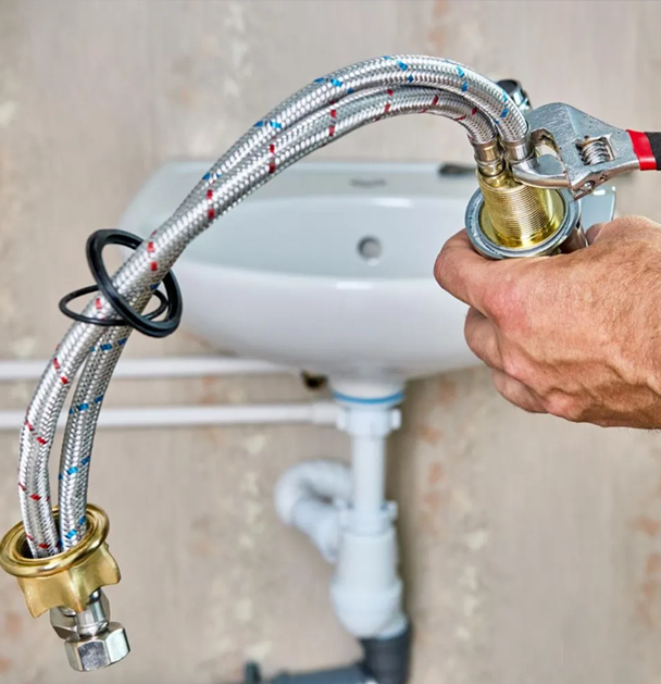 Person using a wrench to tighten a flexible water supply hose to a sink faucet.