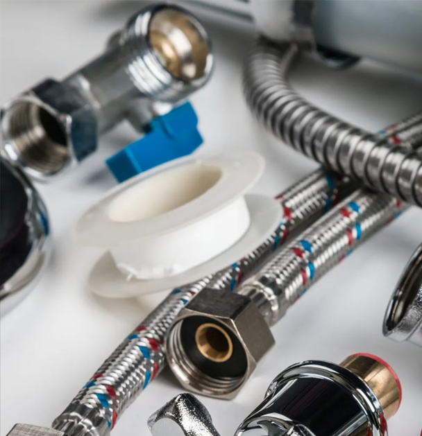 Plumbing hardware close-up: metal fittings, flexible supply lines, Teflon tape, and a blue valve handle.