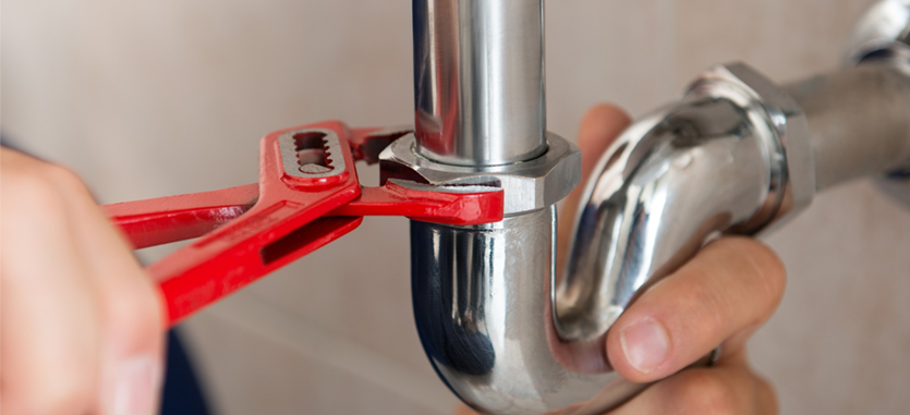 A person using a red wrench to tighten a chrome pipe connection.