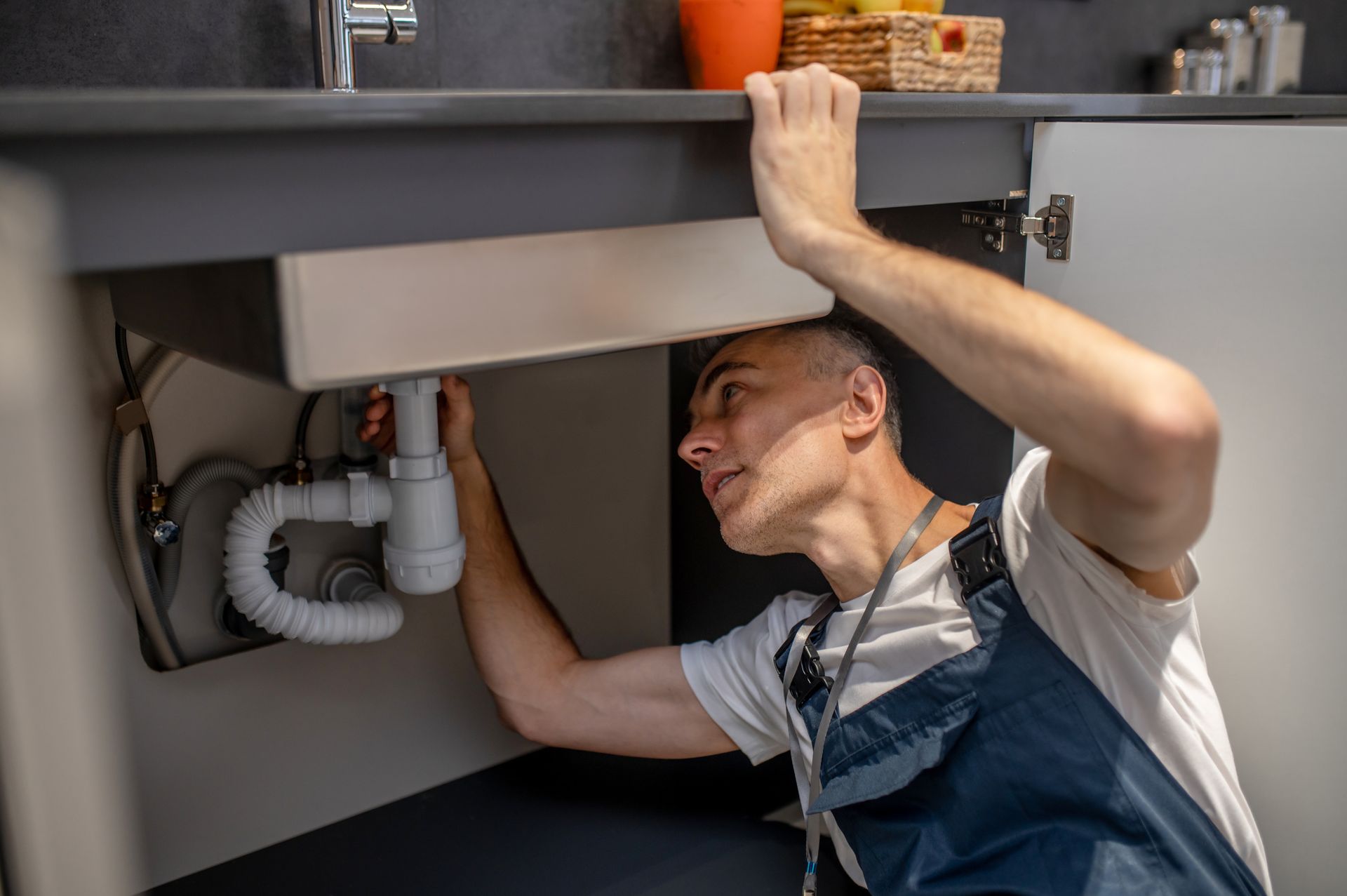 Man fixing plumbing under a kitchen sink.