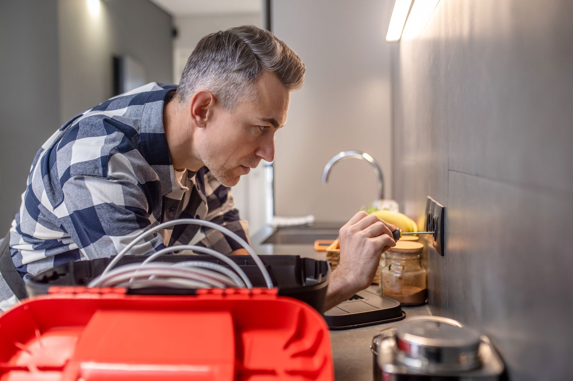 Man working on an electrical outlet, looking intently, with a toolbox.