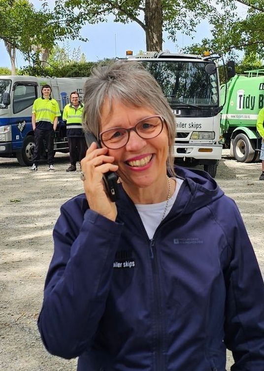 Lynnette from Tidy Bins talking on the phone in front of their team and the garbage truck fleet.
