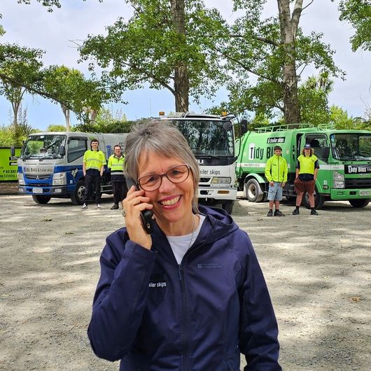 Lynnette from Tidy Bins taking a customer call in front of their garbage truck fleet.