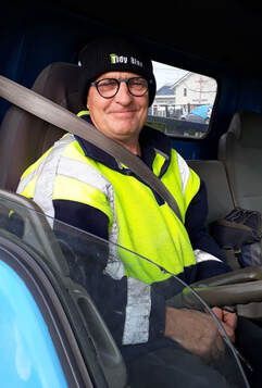 Kevin from Tidy Bins in the driver 's seat of one of their garbage trucks.