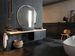 Modern bathroom with dark walls, wooden counter, round mirror, and a small chair.