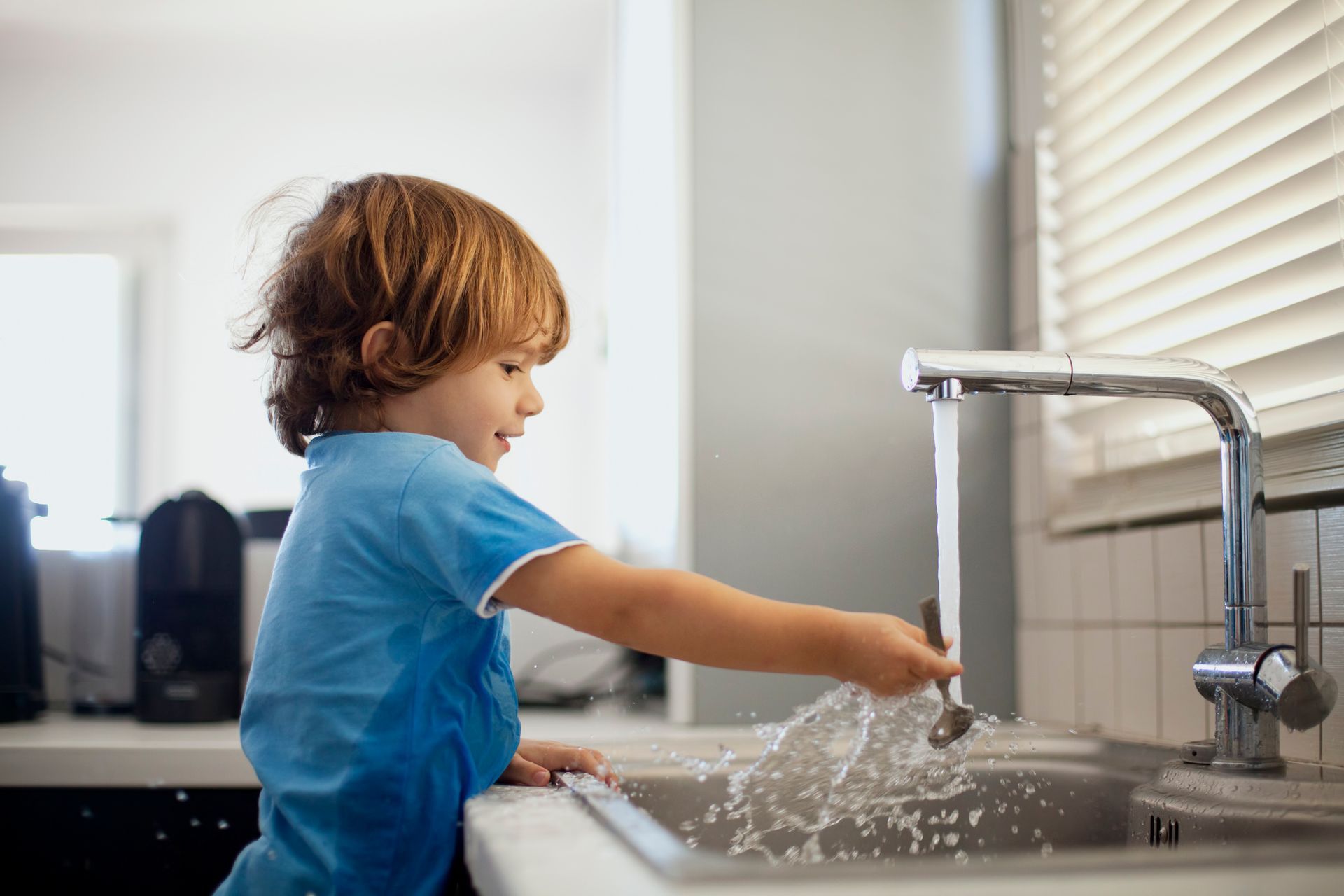 Child playing with running water in a kitchen sink.