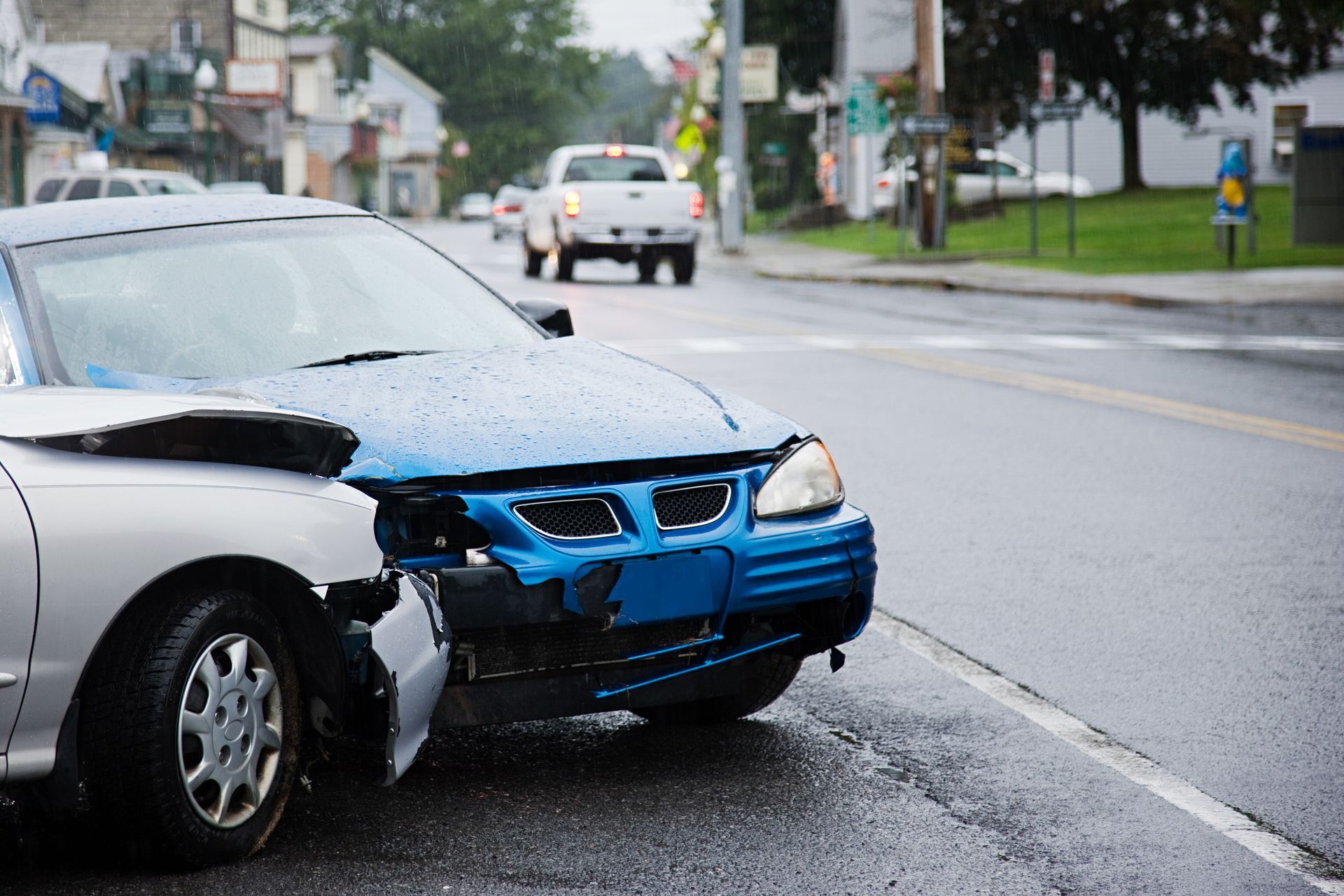 A blue car with a damaged bumper is parked on the side of the road