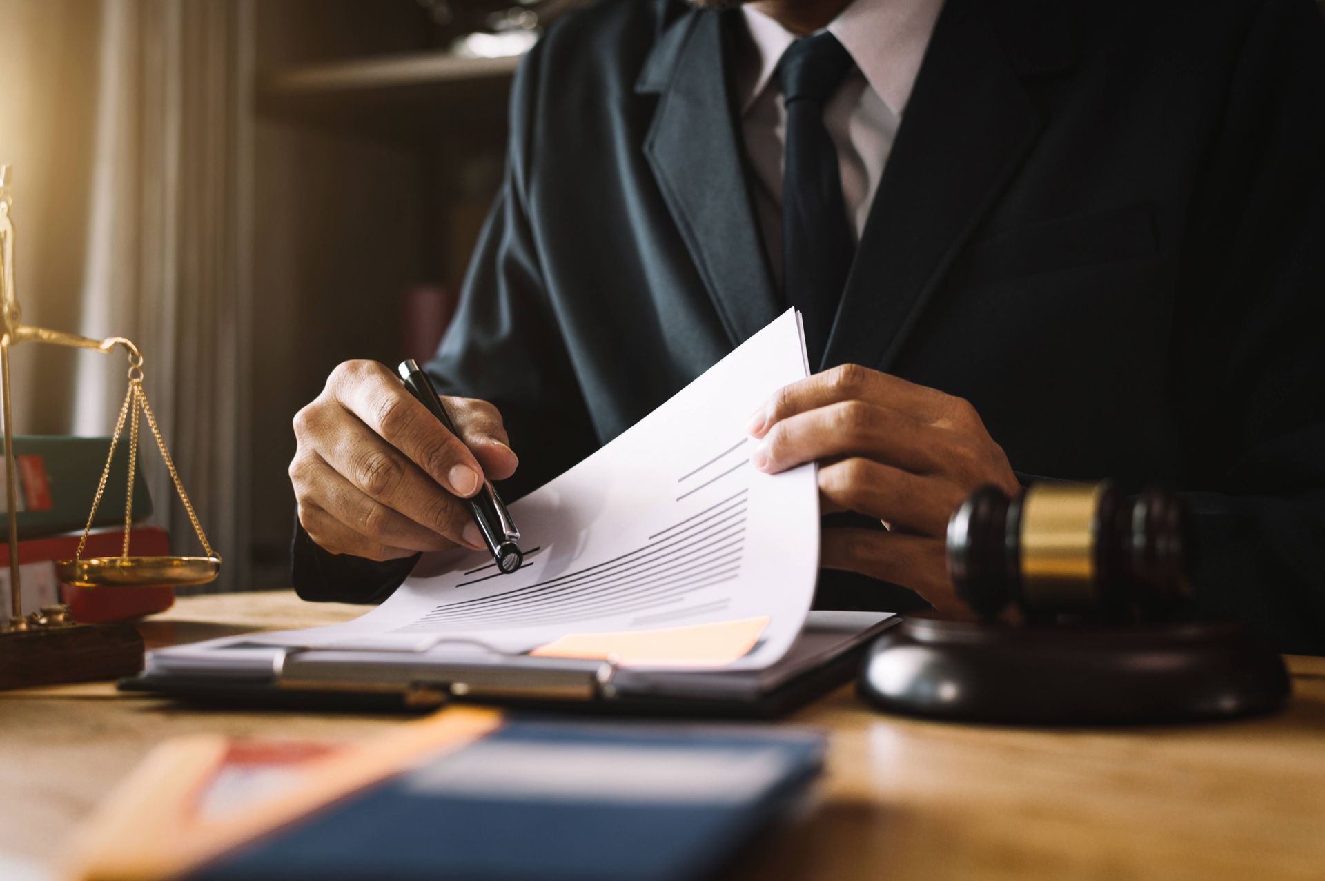 A lawyer seated at a wooden desk with a gavel, books, and scales of justice, checking documents.