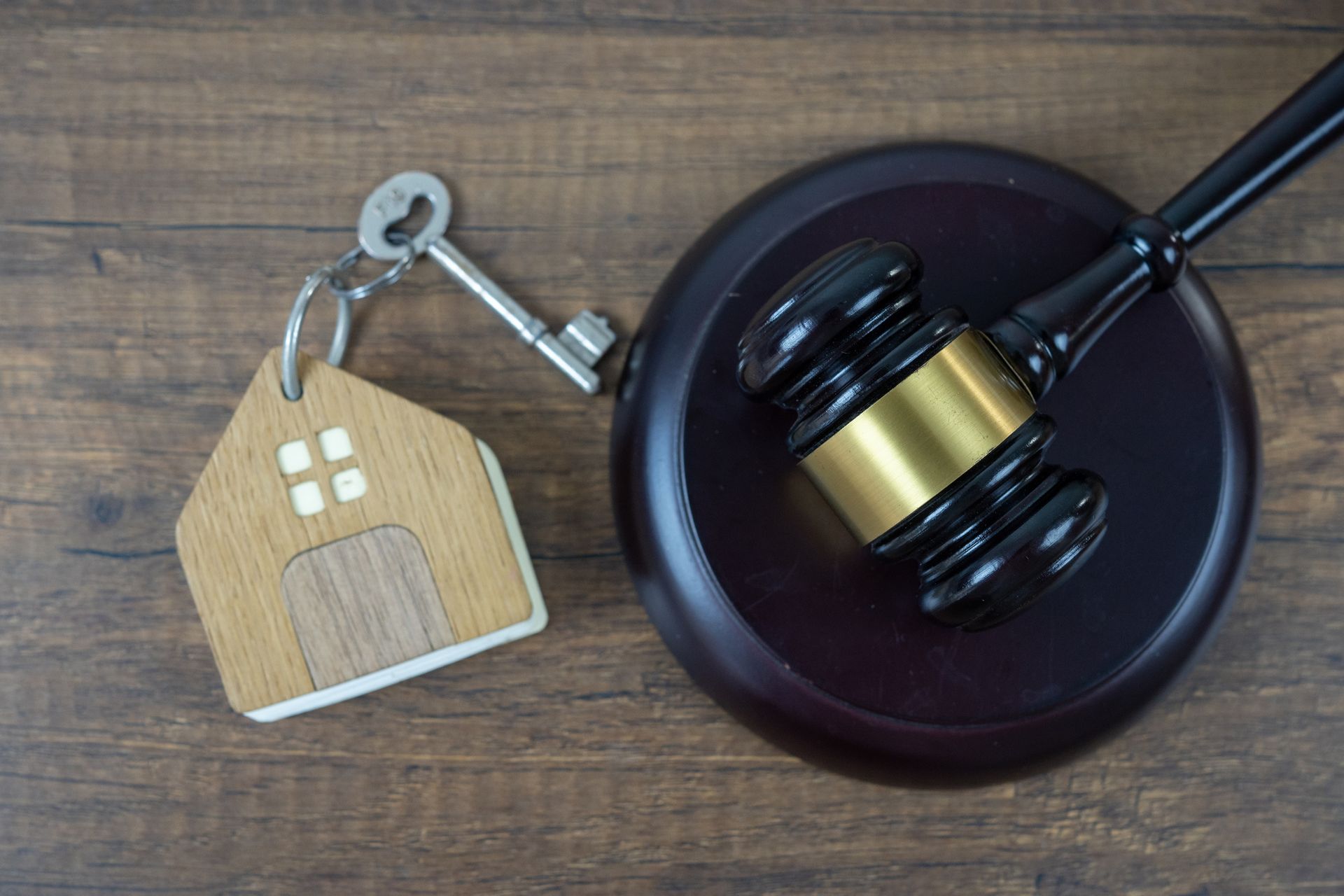 A wooden house keychain and a judge 's gavel on a wooden table.