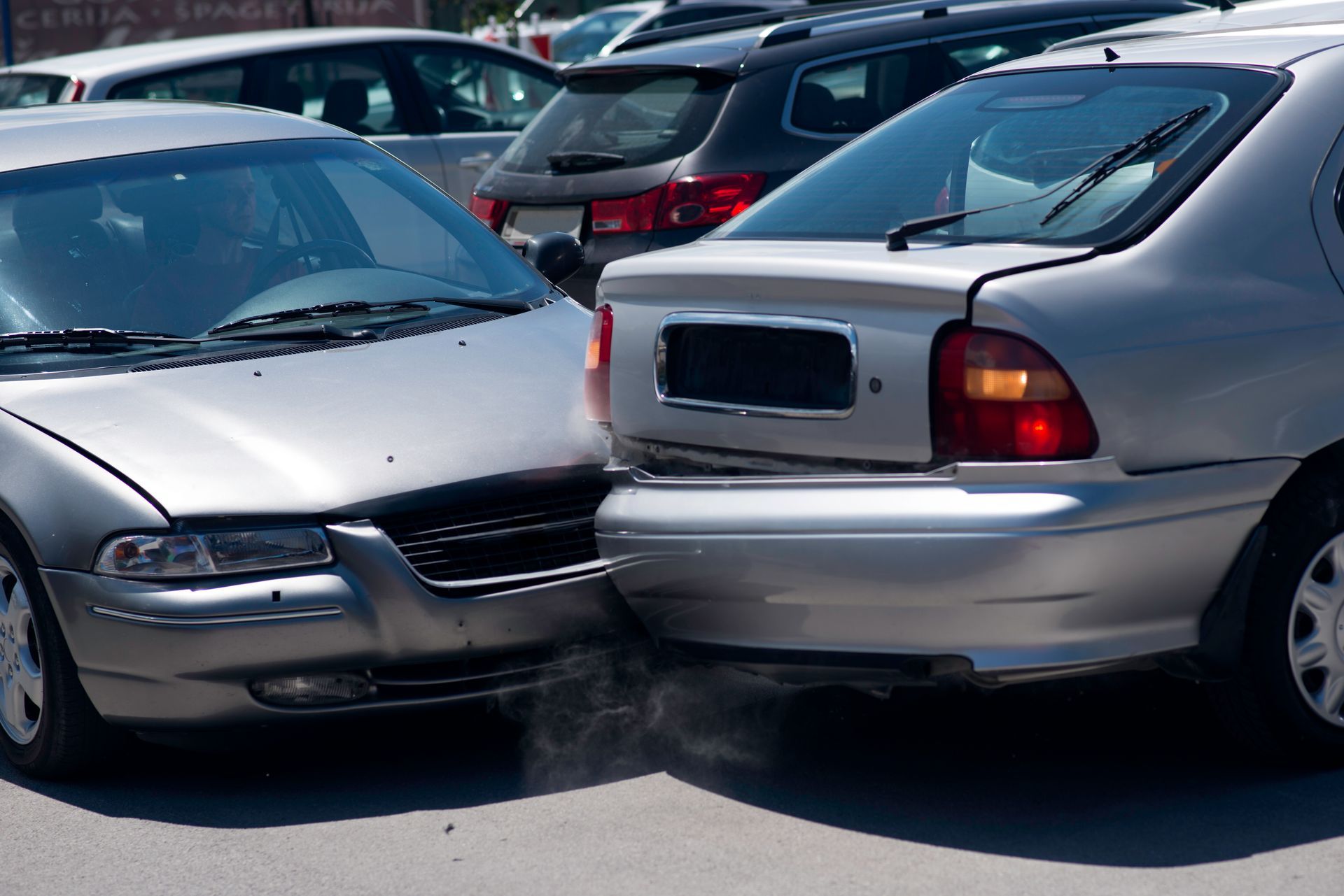 A silver car has crashed into another car in a parking lot