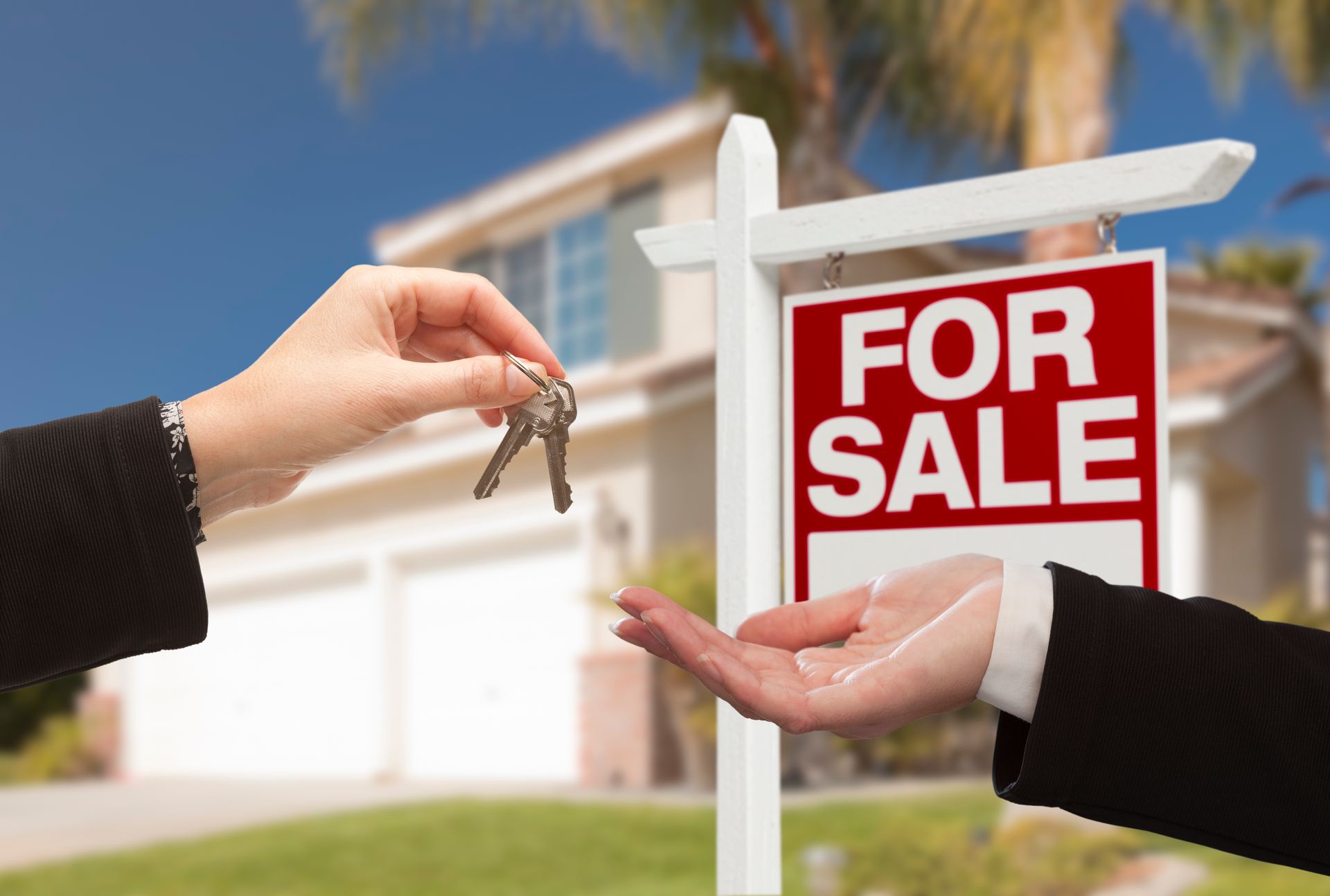 A person is handing keys to another person in front of a for sale sign