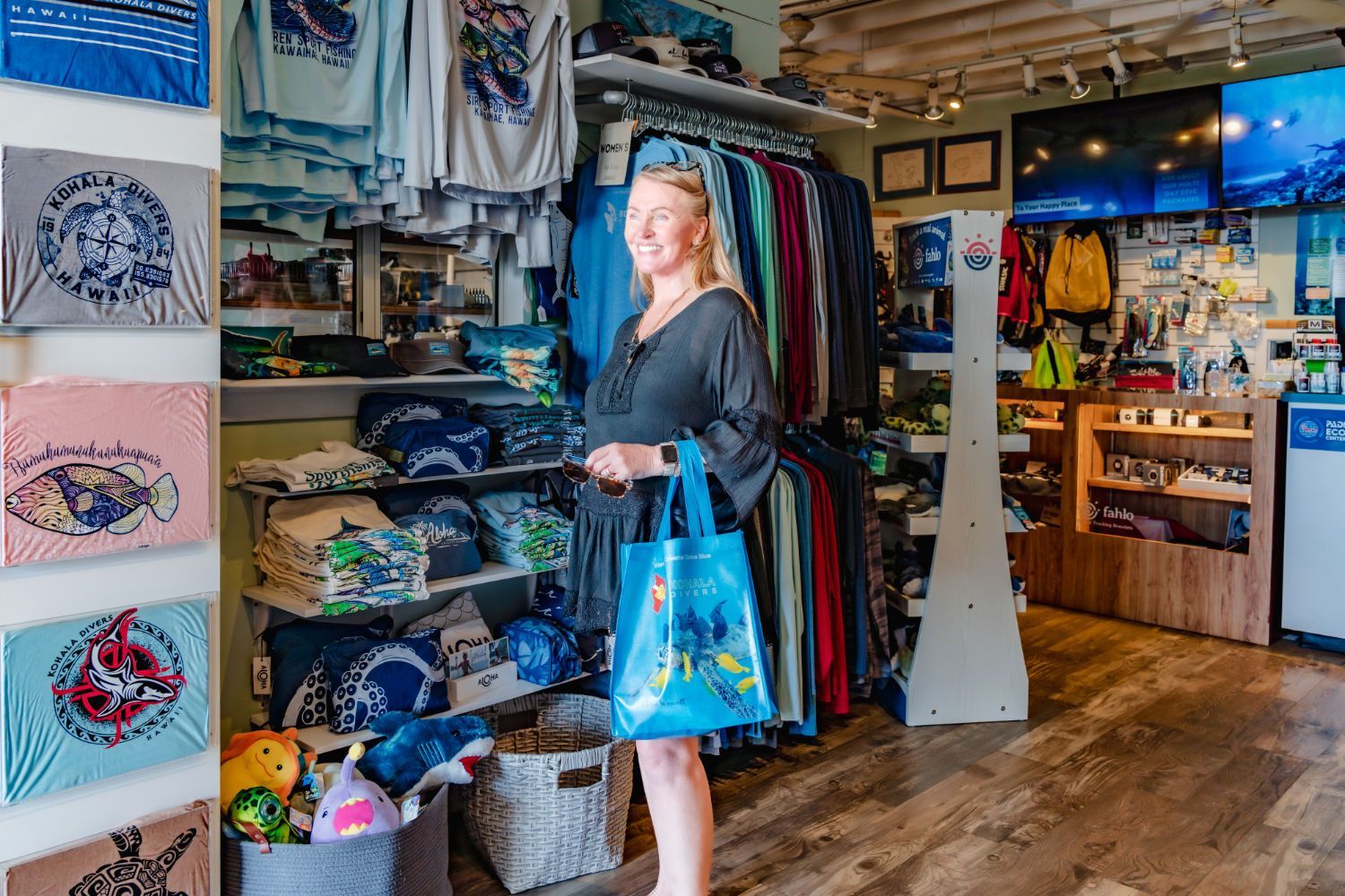 A woman is standing in dive shop holding a blue bag.
