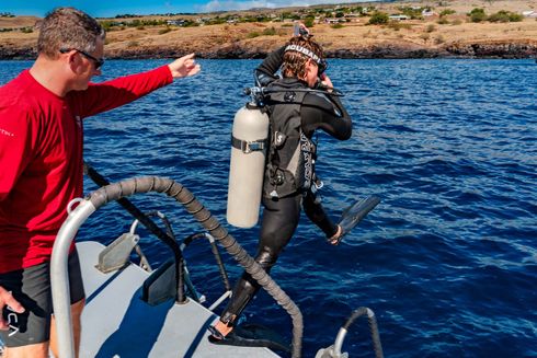A man is pointing at a scuba diver on a boat in the ocean.