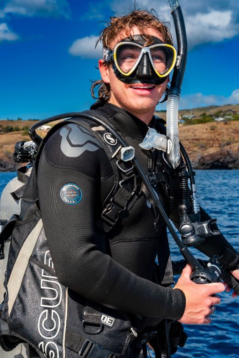 A man in a wetsuit and mask is holding a scuba diving mask.