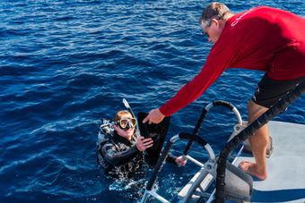 A man is helping a scuba diver out of the water.