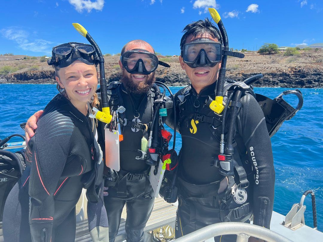 Three scuba divers are posing for a picture on a boat in the ocean.