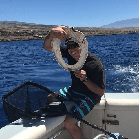 A man is sitting on a boat holding trash from the ocean.
