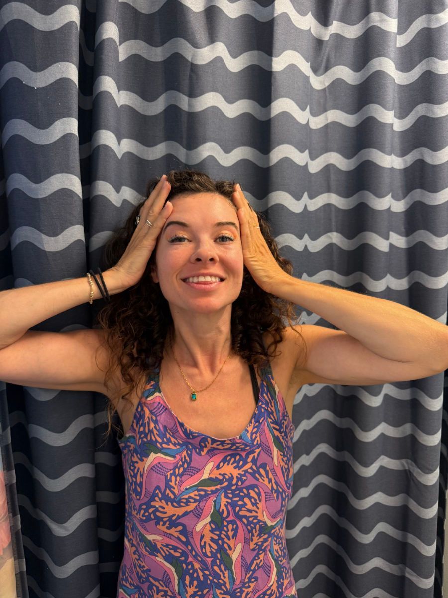 Woman with hands on head, smiling, in front of wavy curtain.