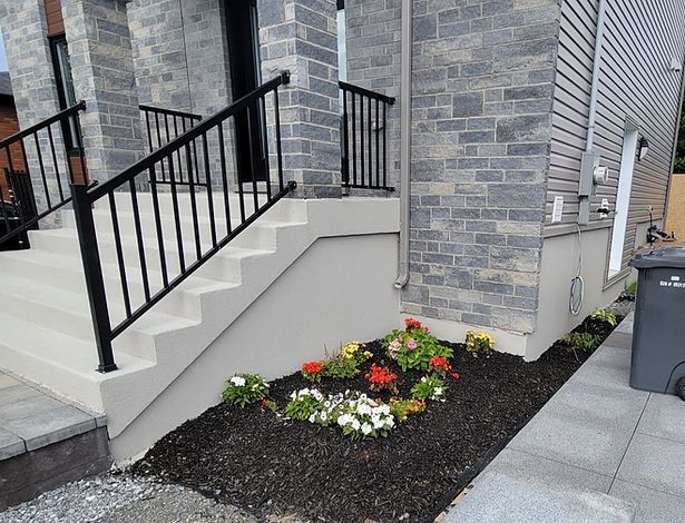 Une maison en brique avec des escaliers et un parterre de fleurs devant.