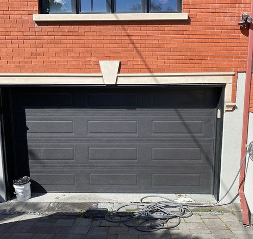 Une porte de garage noire se trouve devant un bâtiment en briques.