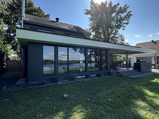 Une grande maison avec beaucoup de fenêtres est située au sommet d'une pelouse verte luxuriante.