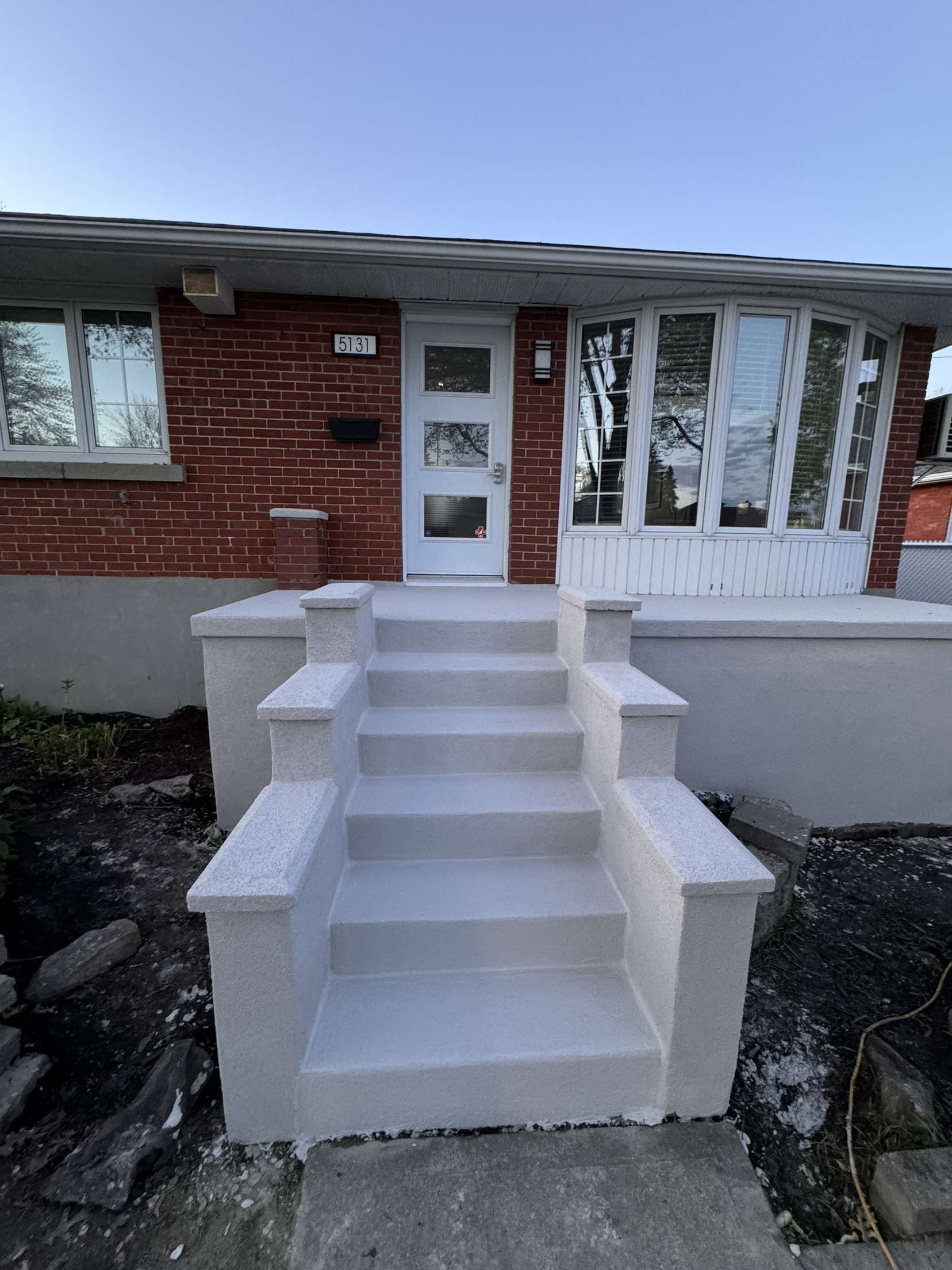 Une maison en briques avec des escaliers blancs menant à la porte d'entrée.