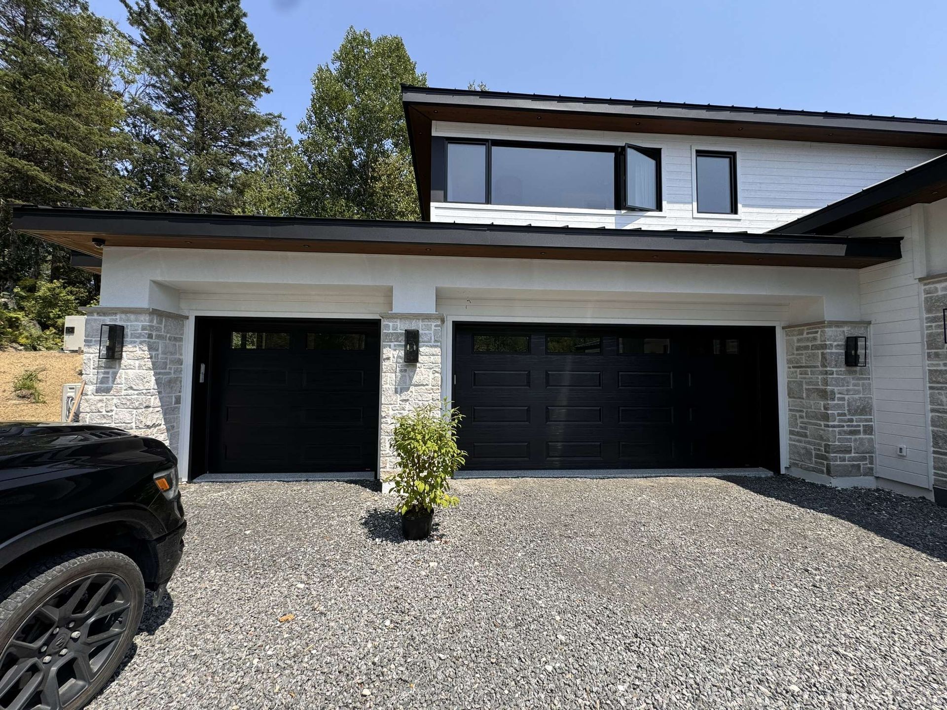 Un camion noir est garé devant une grande maison blanche avec deux portes de garage noires.