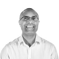 A man wearing glasses and a white shirt is smiling in a black and white photo.