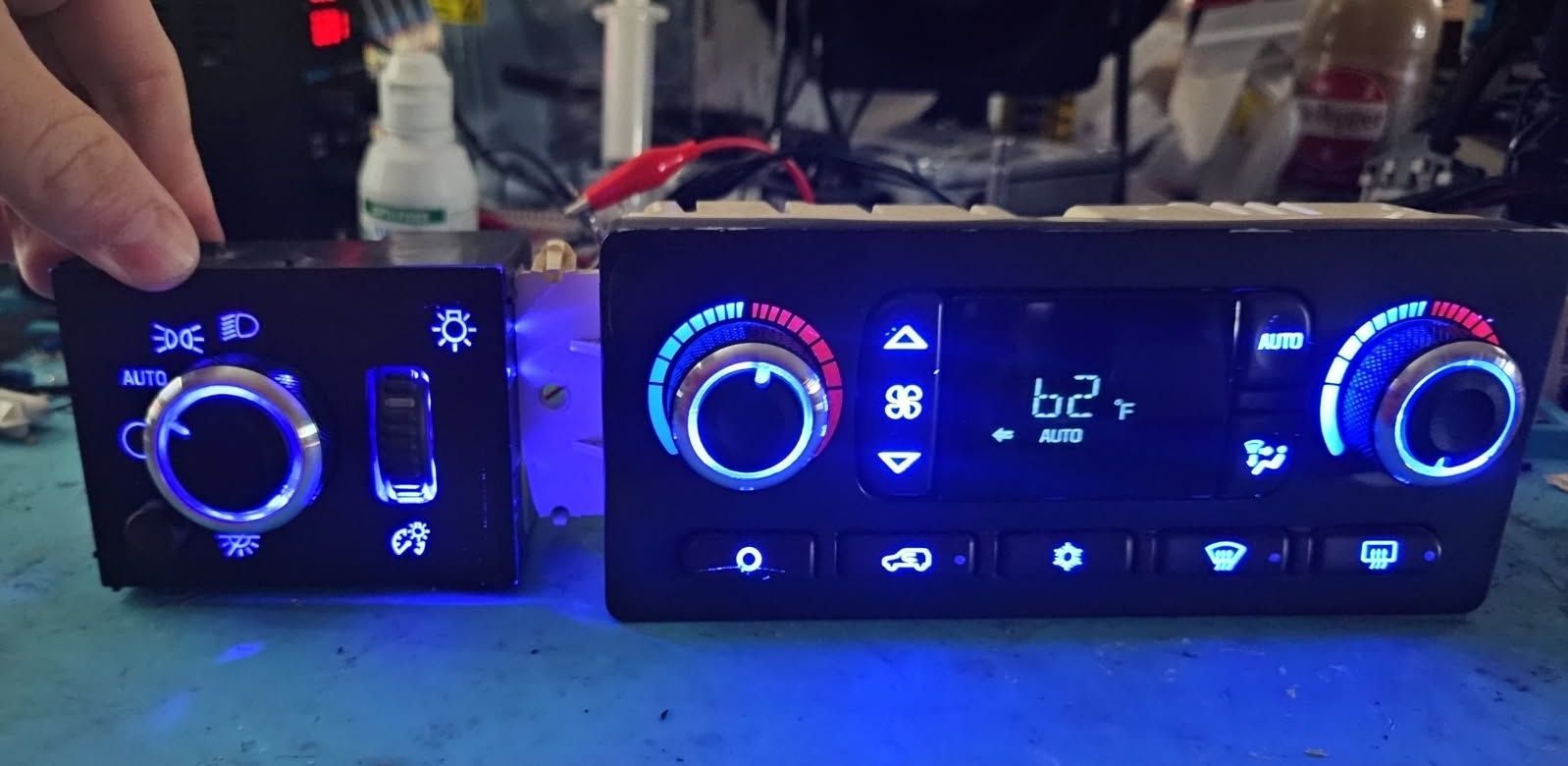 A person is holding a remote control next to a car a/c control panel.