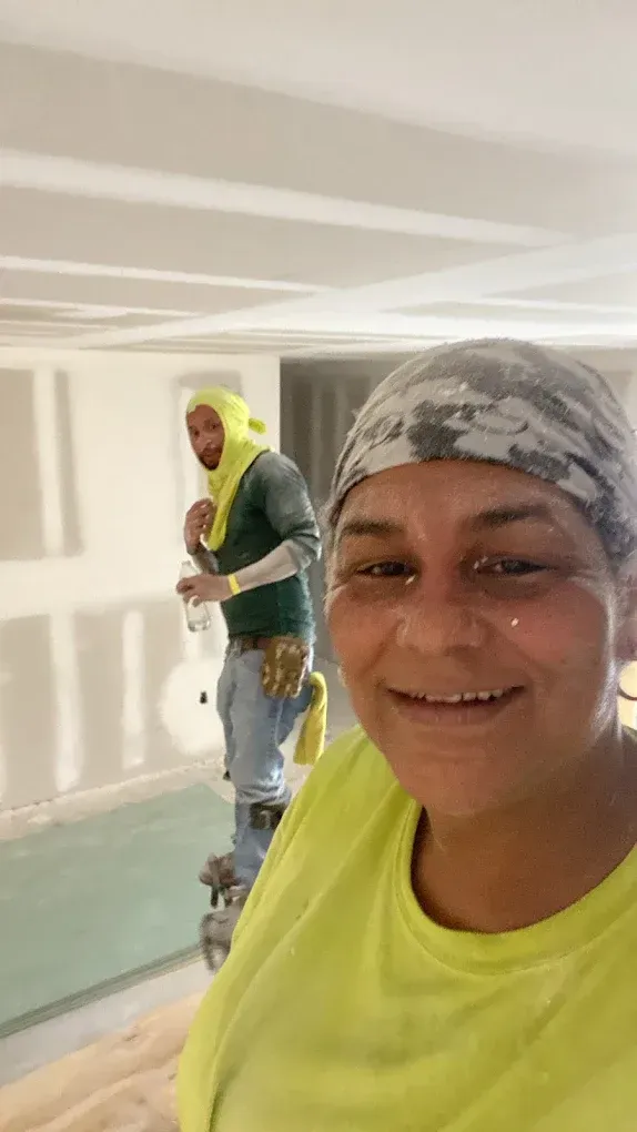 A man and a woman are standing next to each other in a room doing drywall
