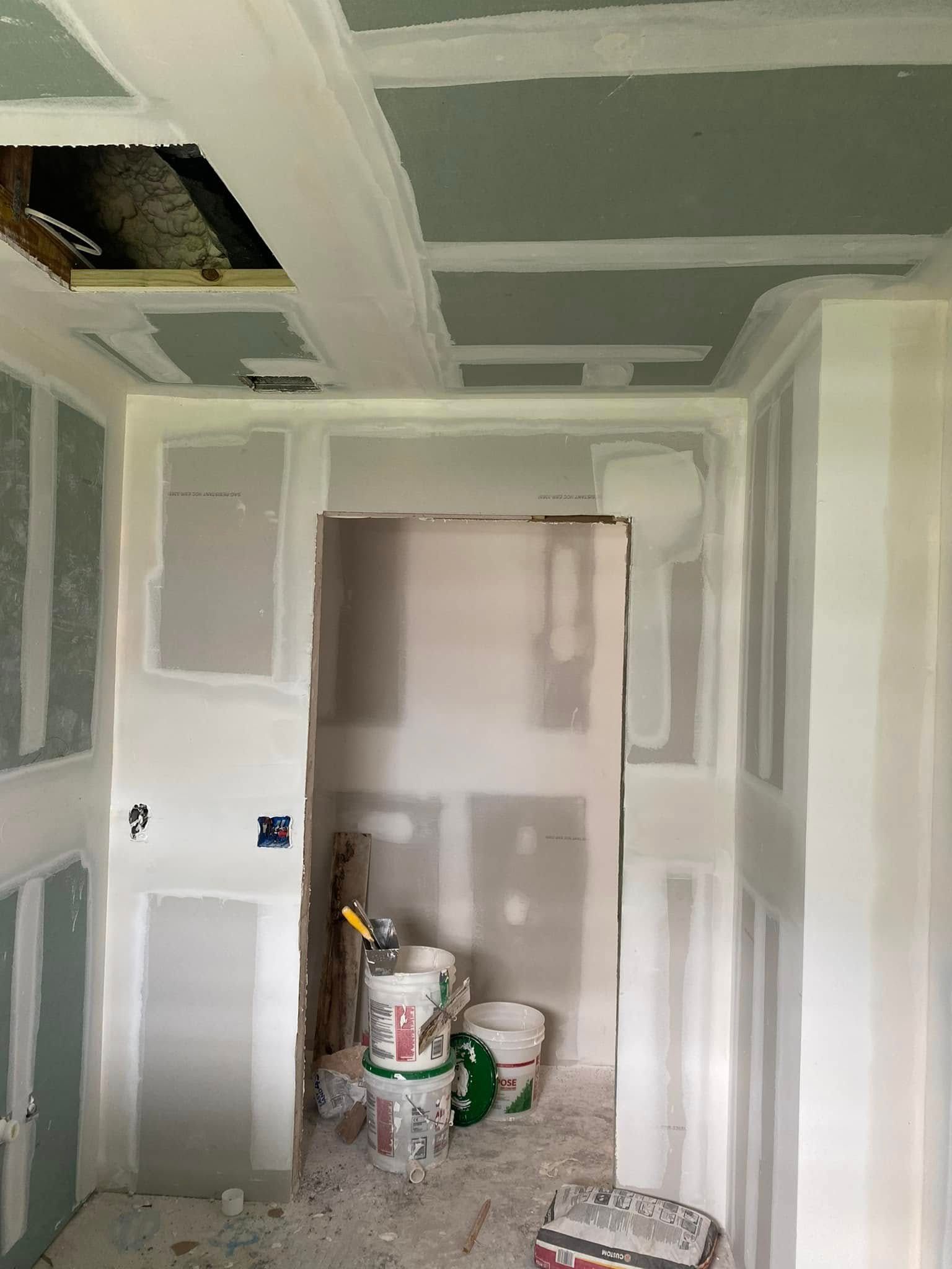 A room with drywall and buckets of paint on the floor.
