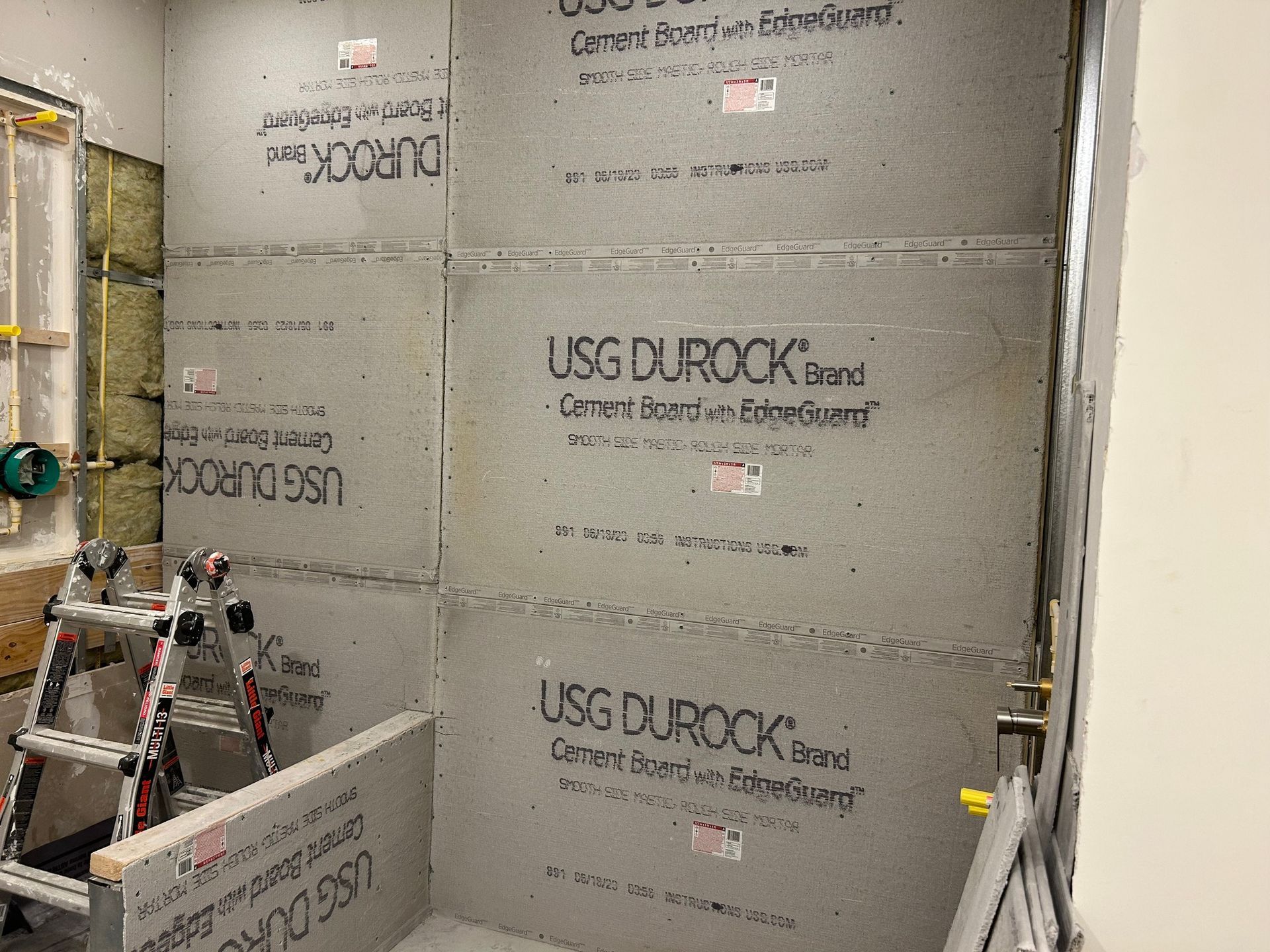 A ladder is sitting in front of a wall with usg durock boards on it.
