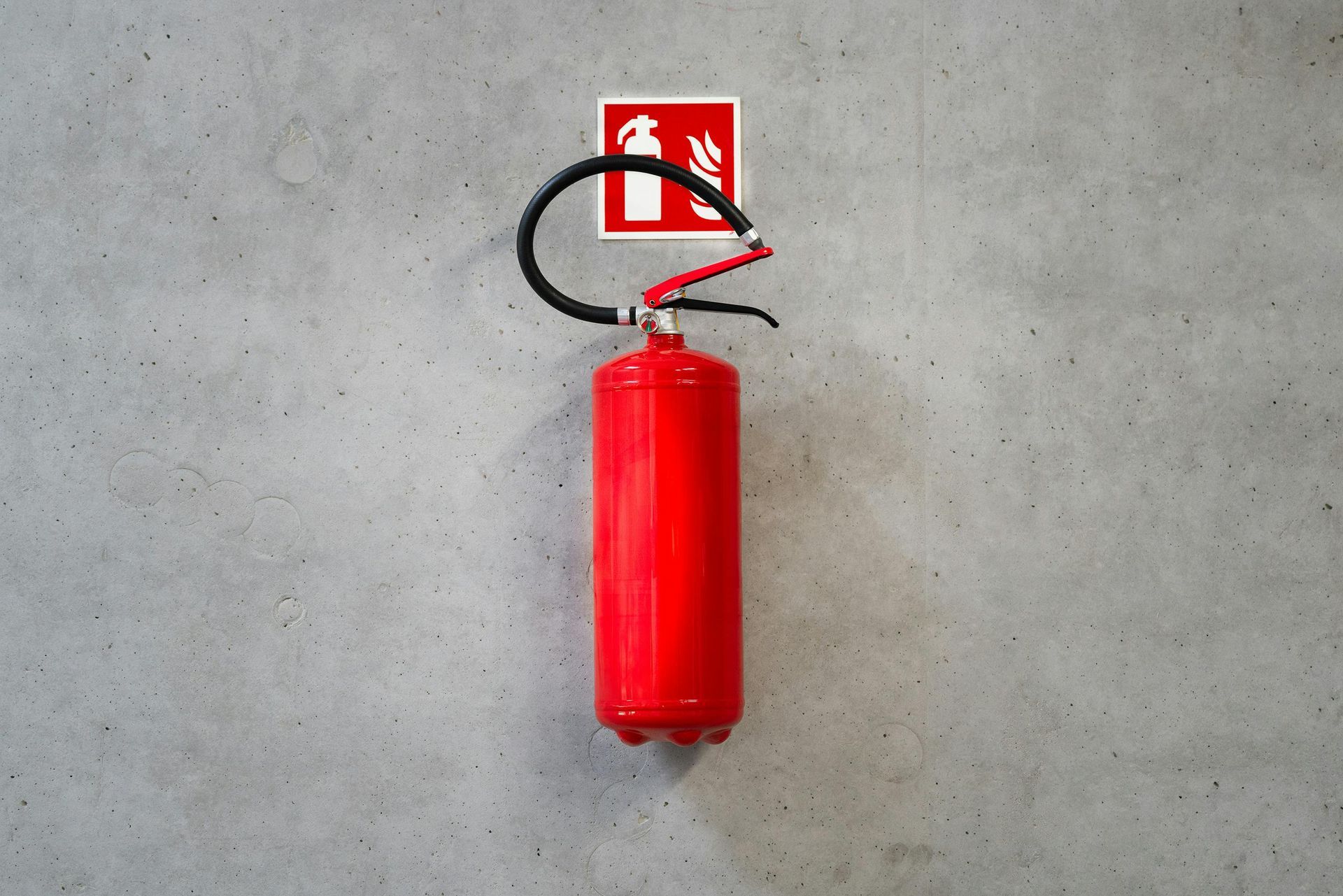 Red fire extinguisher hanging on a gray concrete wall, next to a fire extinguisher sign.