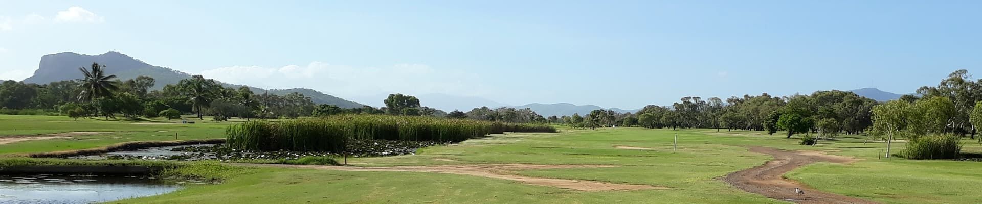 A Dirt Road Going Through A Grassy Field With Trees In The Background — Rowes Bay Golf Club In Rowes Bay, QLD