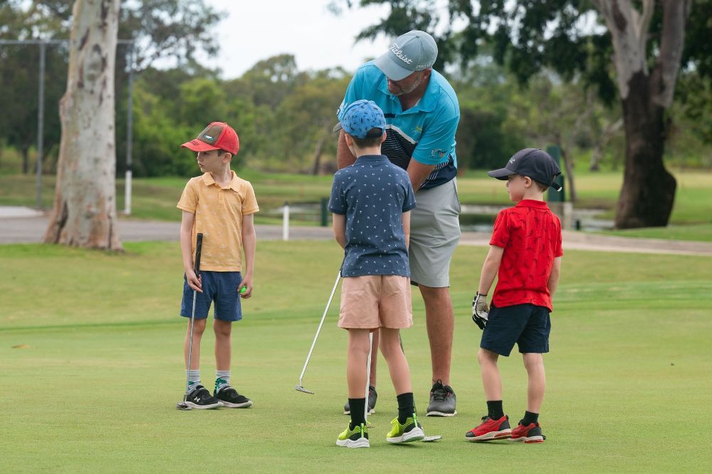 A man is teaching three young boys how to play golf on a golf course.— Rowes Bay Golf Club In Rowes Bay, QLD