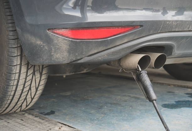 Car exhaust pipes with a probe inserted, likely for emissions testing, at a testing station.