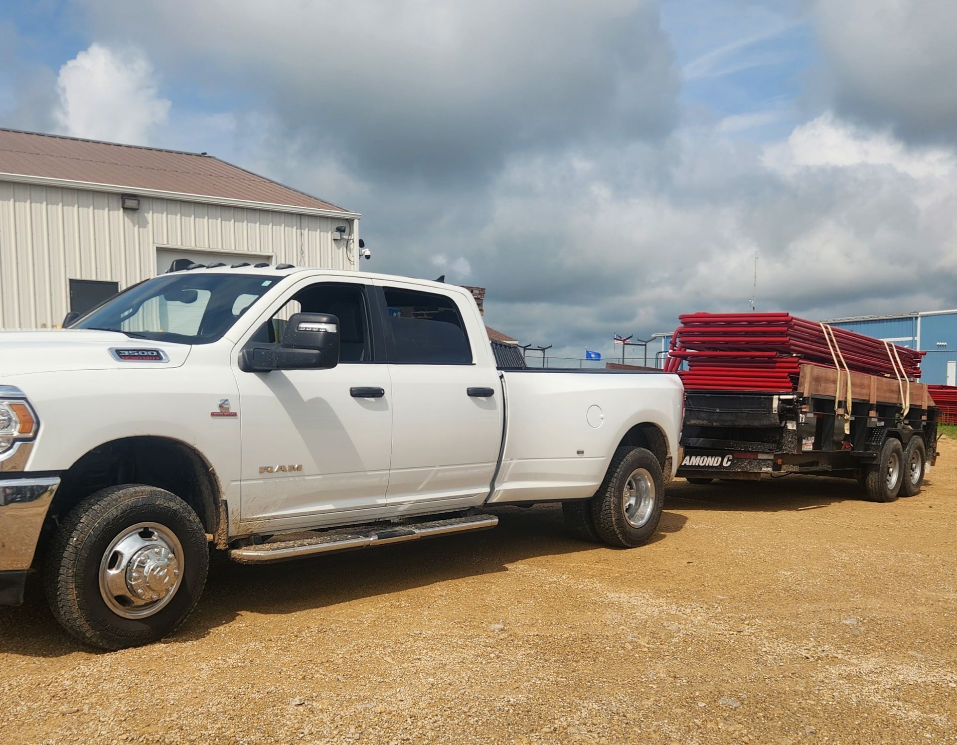 White pickup truck towing a trailer loaded with red metal panels on a gravel lot.