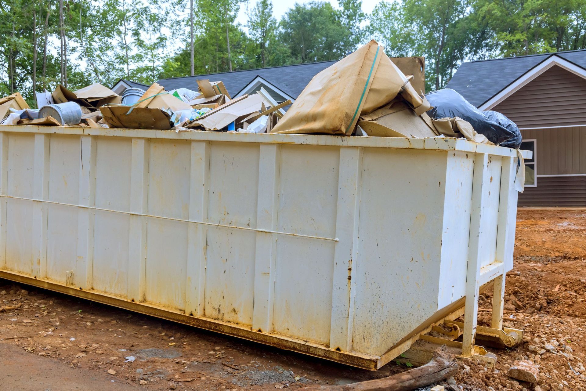 White dumpster overflowing with cardboard and debris at a construction site.