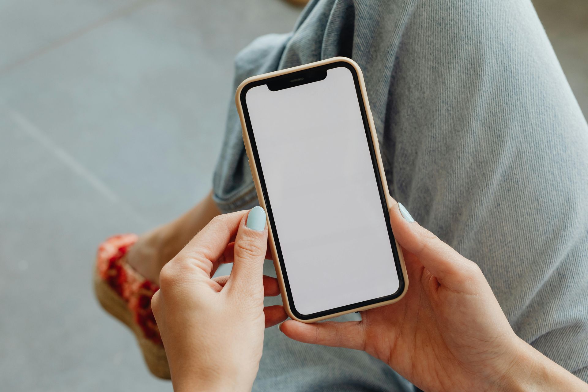 A woman is sitting on the floor holding a cell phone with a white screen.