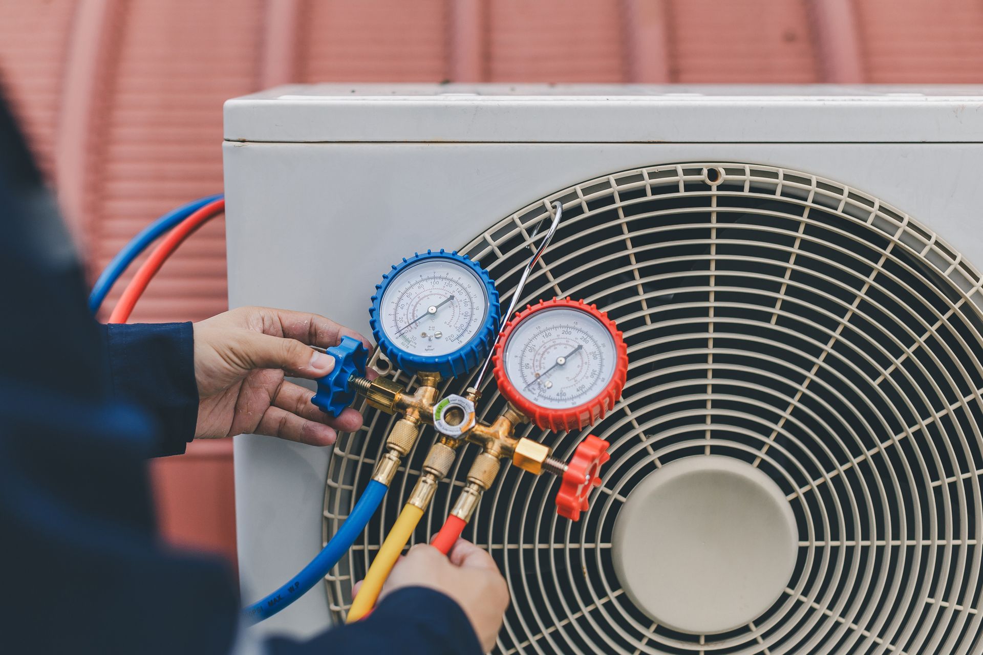 Technician servicing an AC unit, using gauges and hoses connected to the compressor.