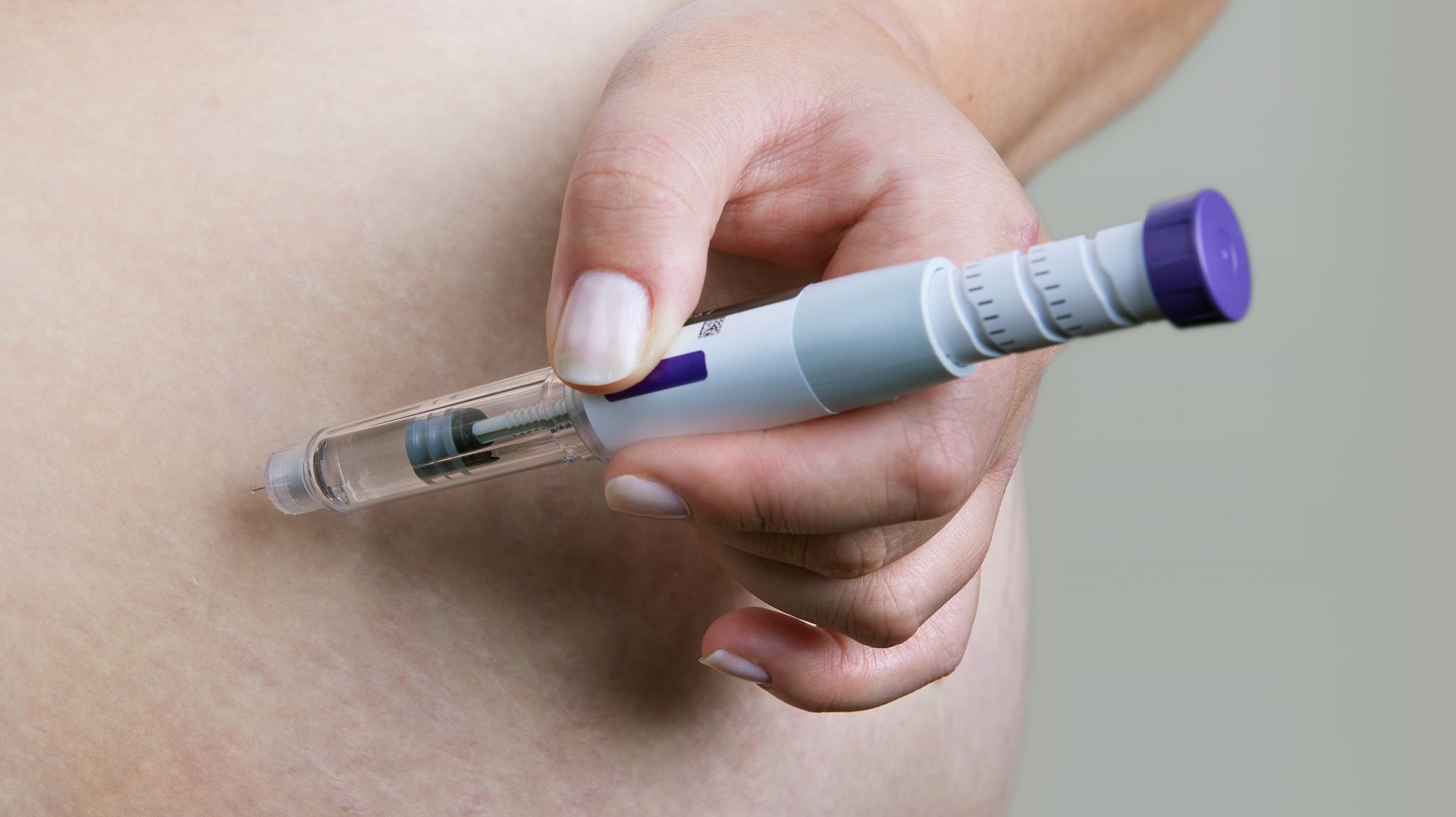 Hand holding a glucose monitor pen against a bare abdomen