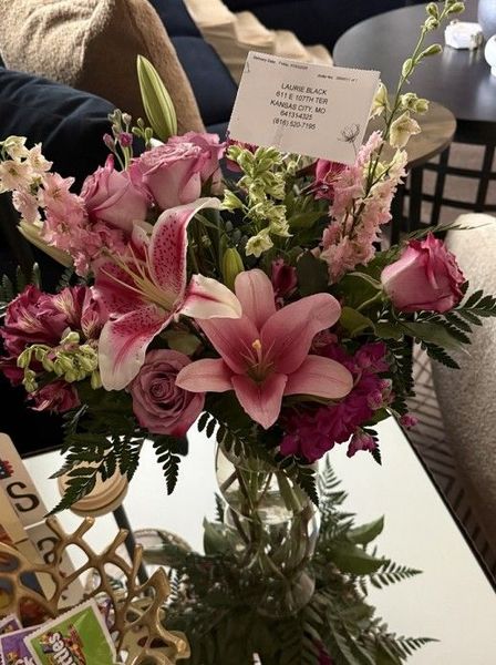 Pink and white flower bouquet in a glass vase on a table with a small card.