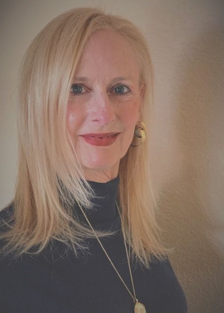 A woman with blonde hair is wearing a black turtleneck and a necklace.