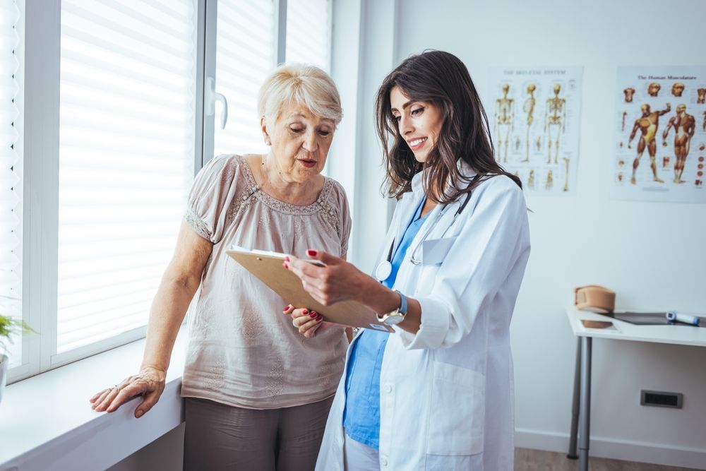 A doctor is talking to an older woman while looking at a clipboard.